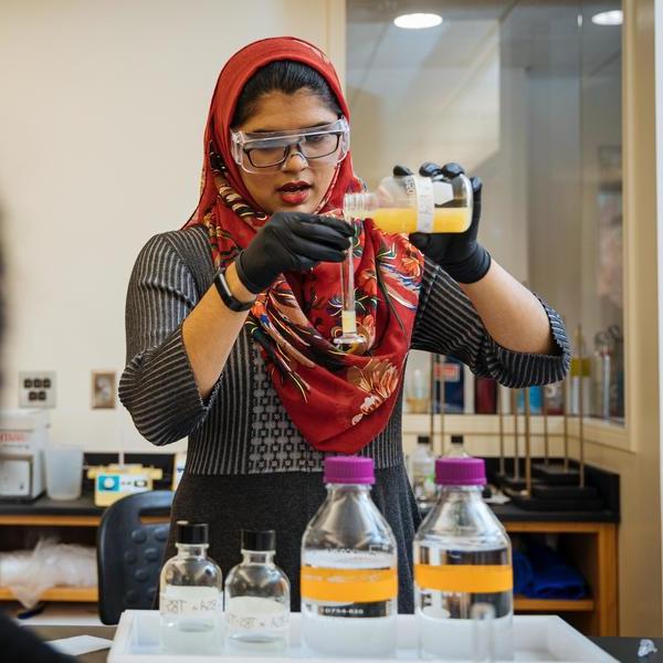 一位戴着彩色头巾的化学专业学生将溶液倒入试管中.